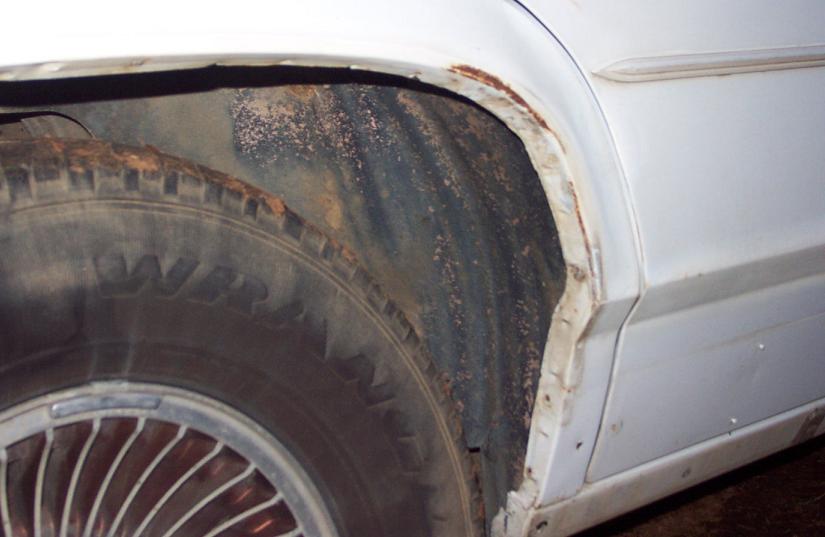 White car's rear wheel well showing significant rust on the fender lip and inner wheel well liner