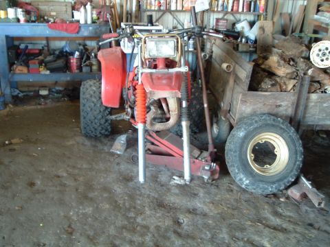 1995 Mercury Grand Marquis - A red three-wheeled ATV is parked in a garage with its front suspension removed, resting on a jack.