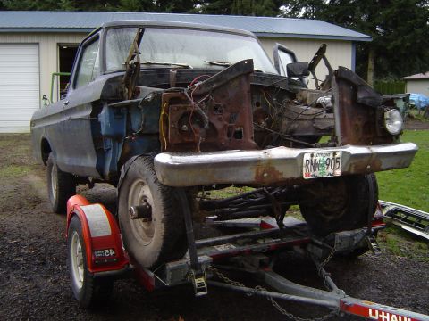 1979 Ford Bronco - This truck, likely a 1973 model, is missing its hood and fenders, revealing a heavily rusted engine bay.