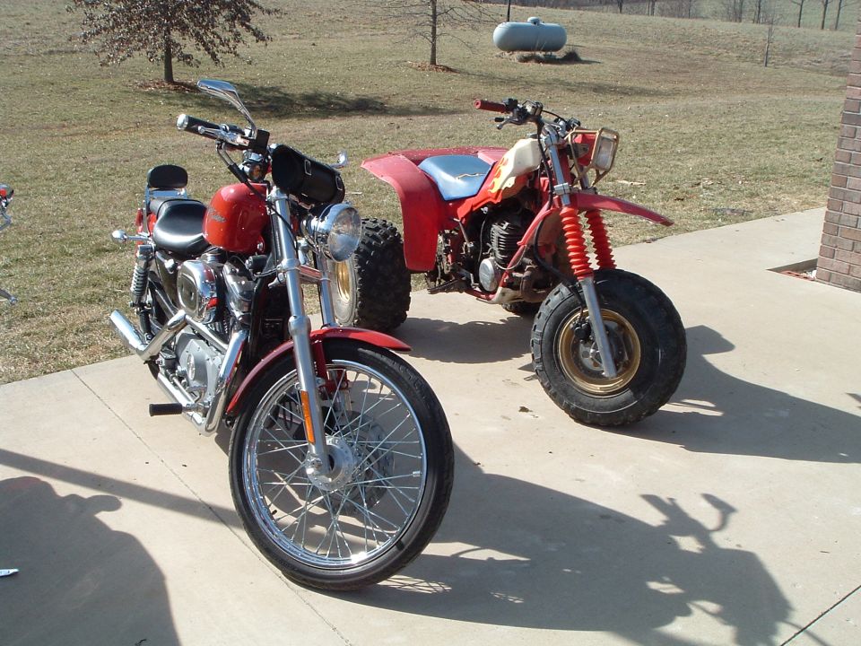 Red motorcycle and red three-wheeler parked on concrete driveway