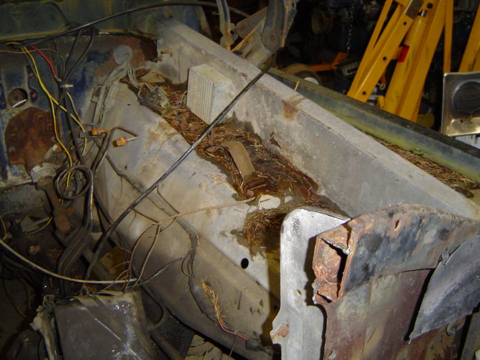 Rusted firewall area of a vehicle, filled with debris and showing exposed wiring