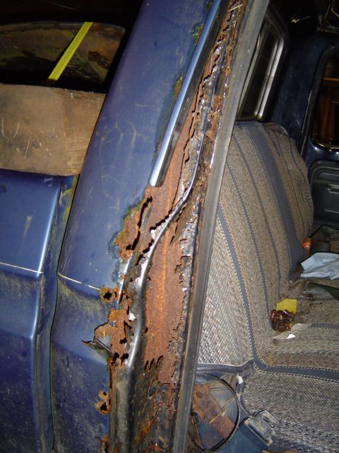 1979 Ford Bronco - Severe rust has consumed the door frame of a blue truck, revealing the interior seat.