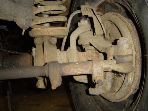 1979 Ford Bronco - Close-up view of a vehicle's front suspension and brake components, including a coil spring and tie rod.