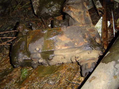 1979 Ford Bronco - A heavily corroded mechanical part, likely from a vehicle, rests on the ground amidst debris.
