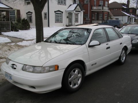 1993 Ford Taurus - A white 1993 Ford Taurus is parked on a residential street with snow on the ground.