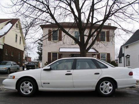 1993 Ford Taurus - A white sedan is parked on a residential street in front of houses during winter.
