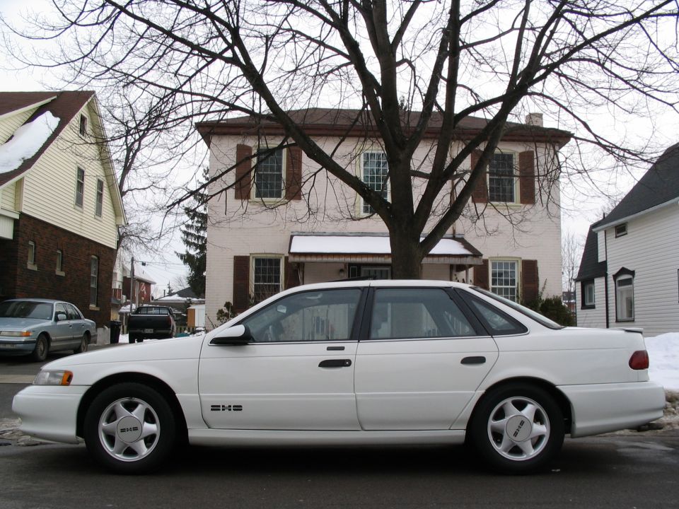White sedan parked on street, side view. Appears to be a 1992 model