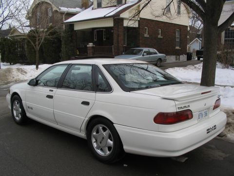 1993 Ford Taurus - A white 1993 Ford Taurus sedan is parked on a street in winter, with a second car visible in the background.