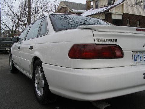 1993 Ford Taurus - Rear view of a white 1993 Ford Taurus sedan with a spoiler and aftermarket wheels.