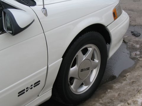 1993 Ford Taurus - The front passenger side of a white 1993 Ford Taurus SHO is visible, showing the wheel and fender.
