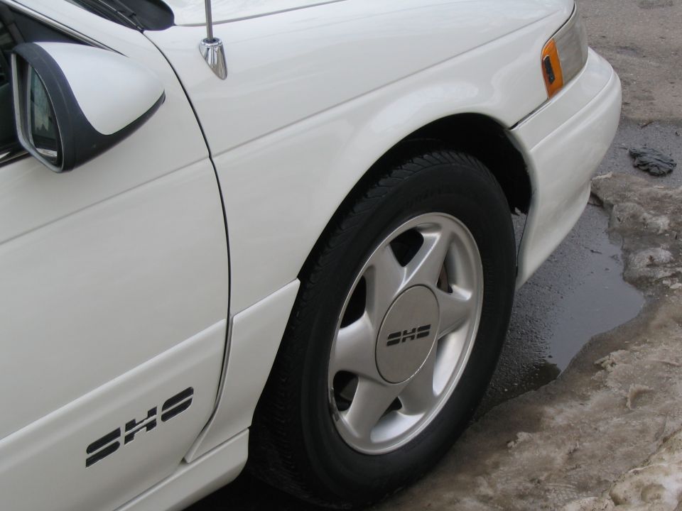 White 1993 Ford Taurus SHO sedan, front passenger side quarter panel and wheel, with a water puddle on the ground