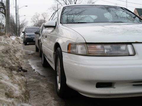 1993 Ford Taurus - A white 1993 Ford Taurus is parked on the side of a street with snow piled on the curb.