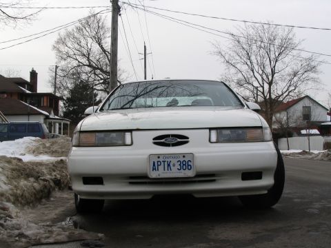 1993 Ford Taurus - A white 1993 Ford Taurus is shown from the front on a cloudy day with snow visible on the roadside.
