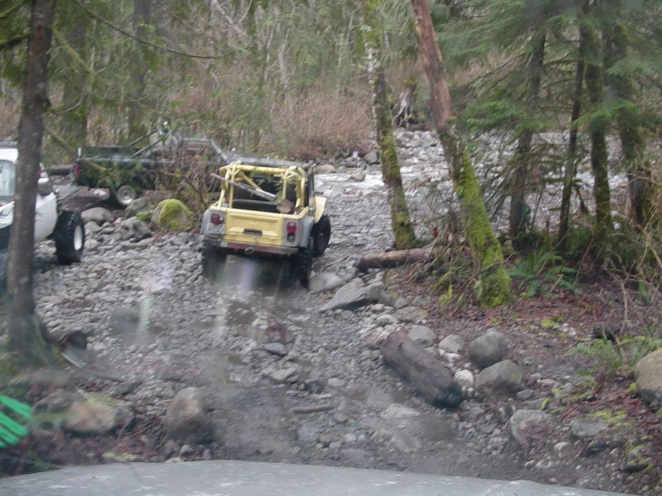 Yellow open-top Jeep climbing a rocky creek crossing in the woods