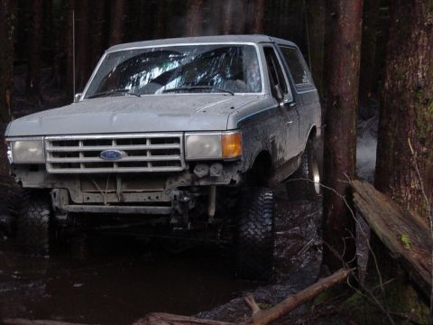1987 Ford Bronco - This 1987 Ford Bronco is navigating a challenging muddy trail surrounded by dense forest.
