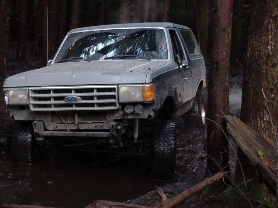 1987 Ford Bronco driving through mud and trees