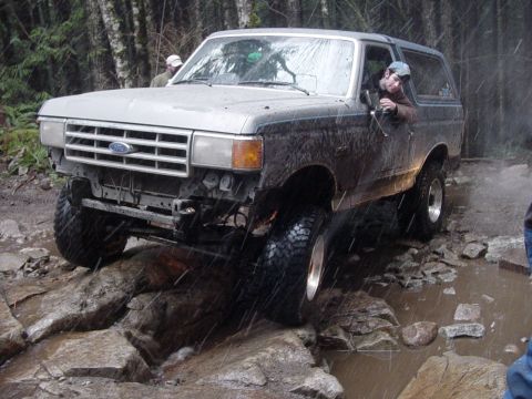 1987 Ford Bronco - A Ford Bronco is shown driving through a challenging rocky and muddy off-road course.
