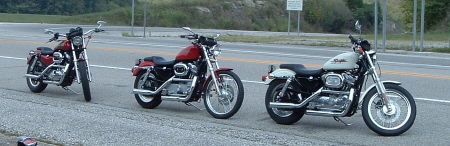1995 Mercury Grand Marquis - Three motorcycles are parked along the roadside on a paved surface.