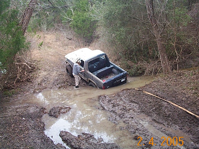 Mud-covered 4x4 stuck nose-down in a water-filled hole on a wooded trail, dated 2.4.2005