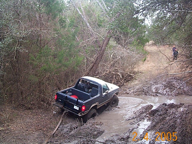 Ford Bronco stuck in a muddy trail, being pulled by a strap