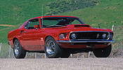 2000 Ford Mustang - This red classic Mustang is parked on a dirt road with a grassy hill behind it.