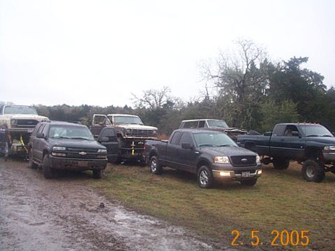 1986 Ford Bronco - A collection of trucks and SUVs are gathered together on a wet, grassy area.