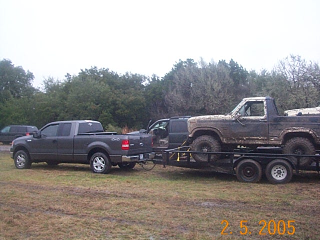 Gray Ford F-150 towing a flatbed trailer with a mud-caked Ford 4x4 on grass