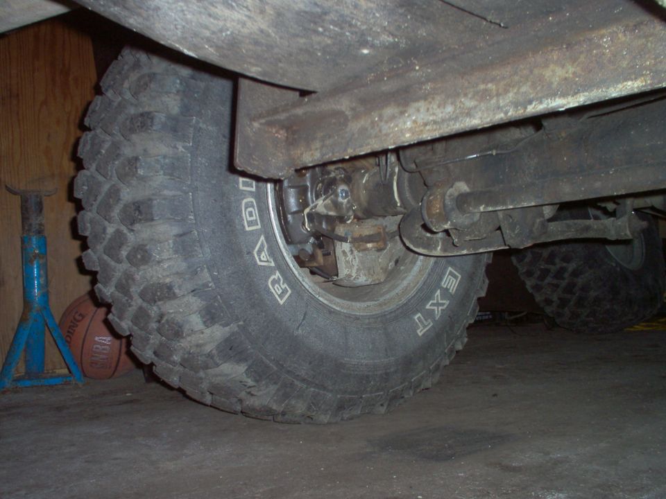 Underbody view of truck front suspension with mud-terrain tire, leaf spring and shock