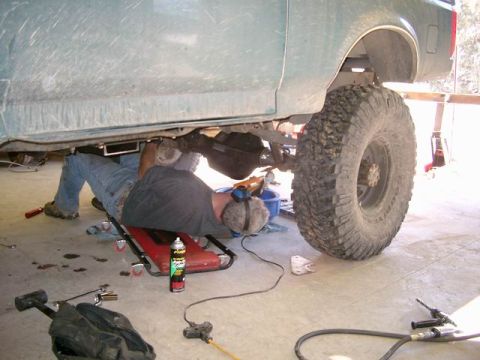 1996 Ford Bronco - A person is working underneath a vehicle, likely performing maintenance or repairs on the rear axle.