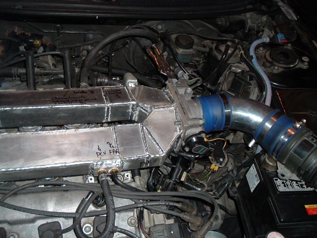 Custom fabricated intake manifold with handwritten notes and PCV fittings, connected to engine components