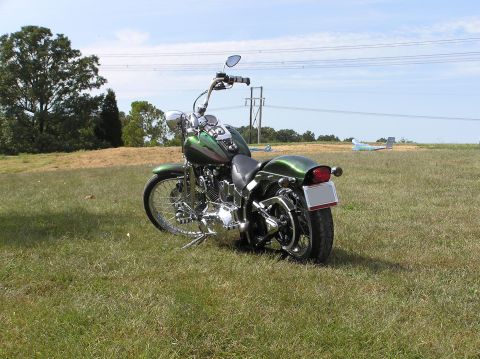 1995 Mercury Grand Marquis - A green motorcycle sits on a grassy field under a bright blue sky with power lines overhead.