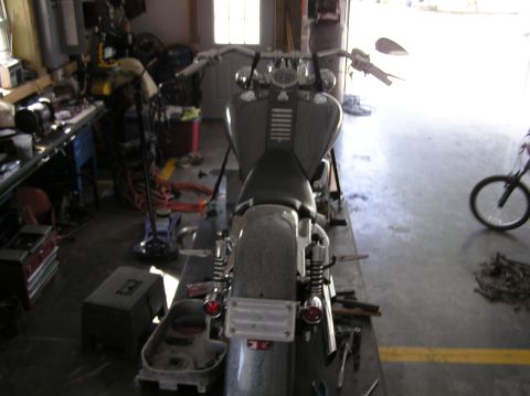 1995 Mercury Grand Marquis - A motorcycle is parked on a lift inside a cluttered garage with tools and equipment around.