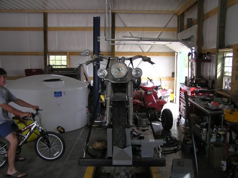 1995 Mercury Grand Marquis - A motorcycle is centered on a lift in a garage, with an ATV and a bicycle also visible.