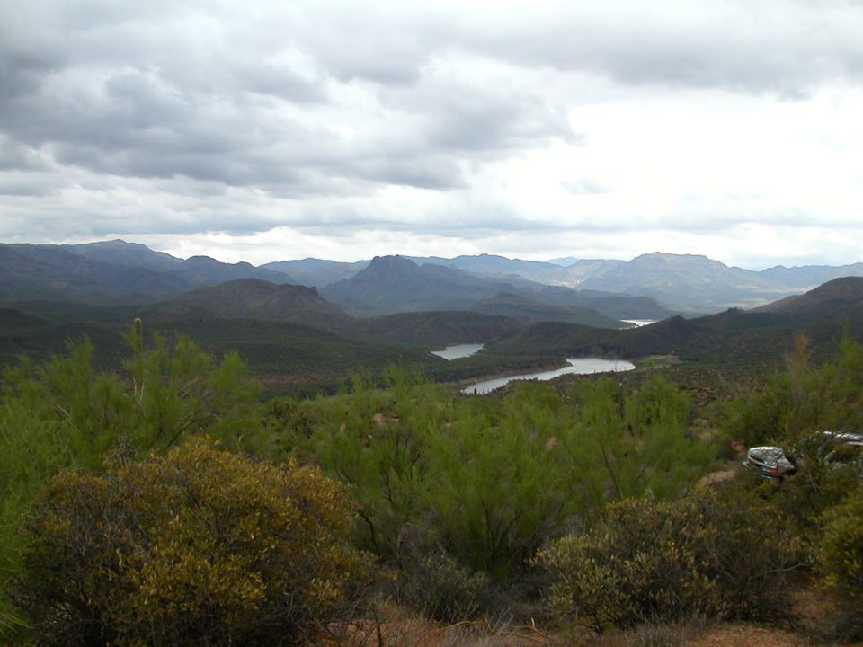 Mountainous terrain with two lakes under a cloudy sky; a vehicle is partially visible on the right