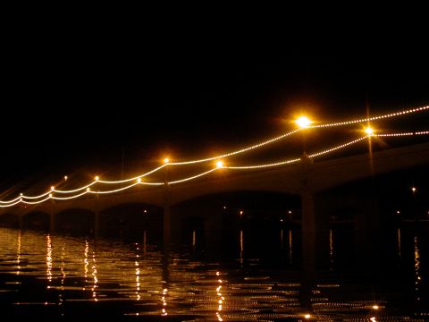 1993 Ford Bronco - A bridge illuminated by strings of lights at night, with its reflection shimmering on the water below.