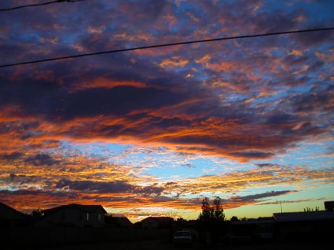 1993 Ford Bronco - A dramatic sunset paints the sky with vibrant colors over a residential area, with a single vehicle barely visible in the distance.