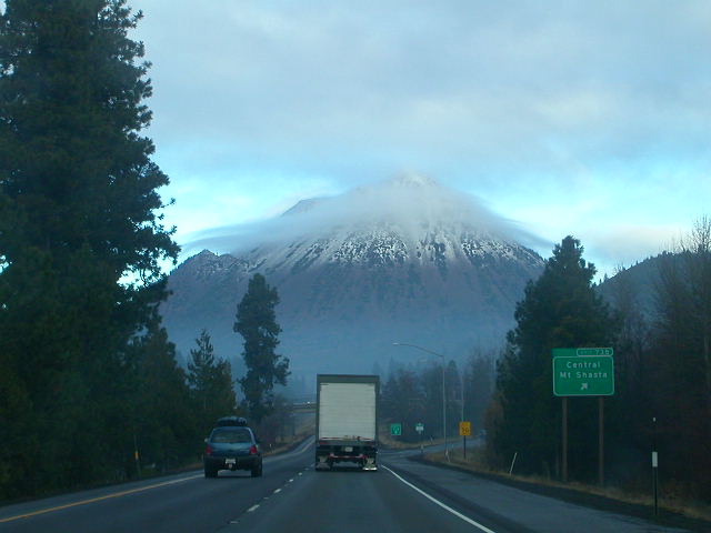 Highway driving towards a snow-capped mountain, with a truck and car on the road