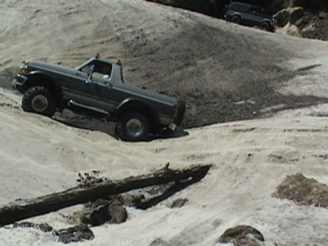 1992 Ford Bronco - A 1992 Ford Bronco navigates a challenging sandy terrain, with another vehicle visible on the higher ground.