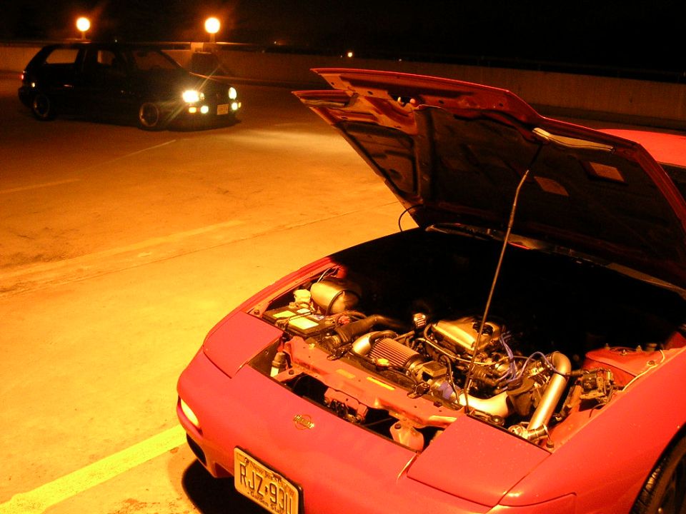 Red Nissan 240SX with hood open showing turbo engine swap at night