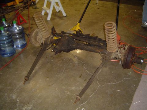 1979 Ford Bronco - A disassembled front axle assembly, including springs and brake components, lies on a concrete floor.