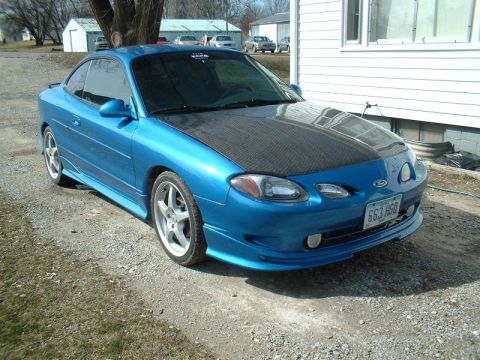 2000 Ford Escort - A blue 2000 Ford Escort ZX2 coupe is parked outside on a gravel driveway, a carbon fiber hood and custom body kit.