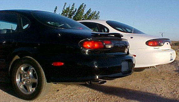 Black sedan and white sedan parked on dirt lot, rear view