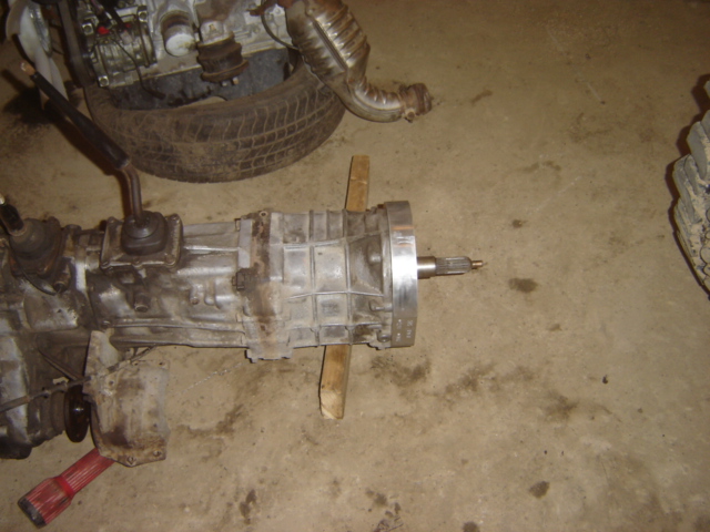Transmission and engine parts on a concrete floor. A red tool is visible