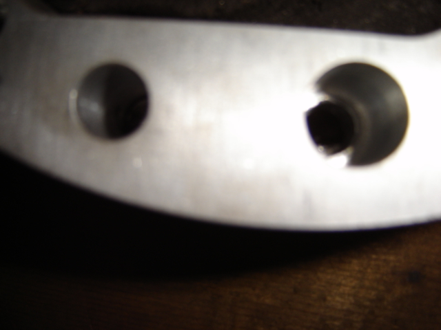 Close-up of a metal bracket with two circular openings, one on the left and one on the right. Text at the bottom reads SUPERMOTORS