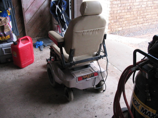 Rear view of a tan Jazzy power wheelchair parked in a garage beside a red gas can