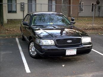 2001 Ford Crown Victoria - This black 2001 Ford Crown Victoria is parked in a lot. The front of the vehicle is visible.