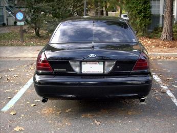 2001 Ford Crown Victoria - The rear of a black 2001 Ford Crown Victoria is visible, parked in an outdoor lot.