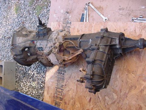 1995 Ford Bronco - Transmission and transfer case assembly removed from a vehicle, resting on plywood with wrenches nearby.