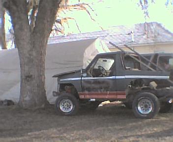 1983 Ford Bronco - Side view of a dark gray Ford Bronco with a red stripe, showing its interior and roll cage.