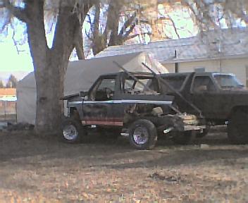1983 Ford Bronco - A black SUV with a prominent roll cage and custom rear modification is parked outdoors next to another vehicle.